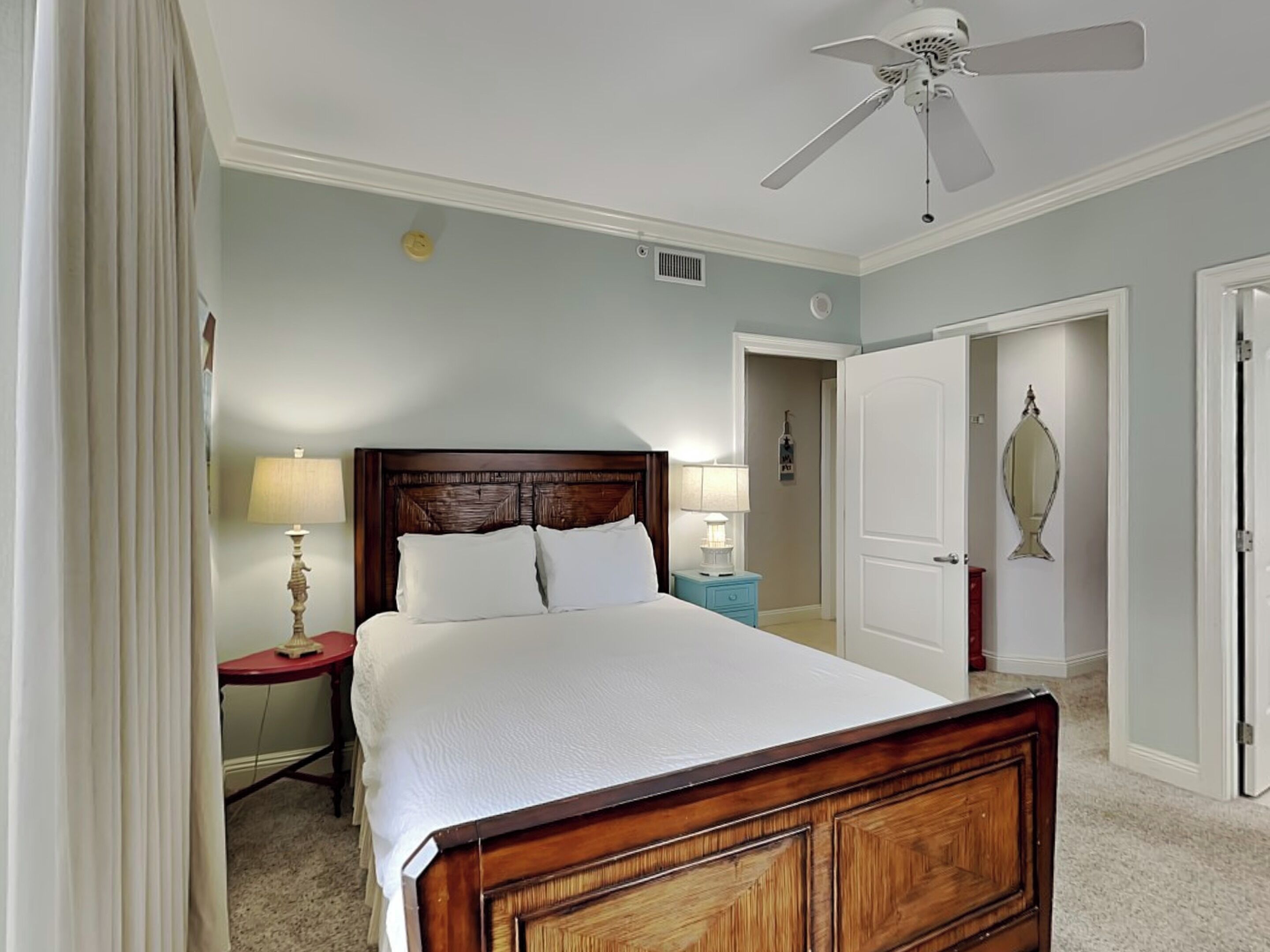 A neatly arranged bedroom with a large bed, a nightstand, a lamp, and a ceiling fan.