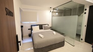 Camera moderna con un ampio letto, cabina doccia in vetro e porta del bagno a vista.