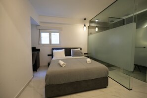 A modern bedroom with a large bed, a desk, and a glass partition. - Signature Suites - Stadiou (Athens)