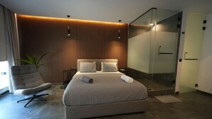 Un dormitorio moderno con una cama grande, una silla, cabina de ducha de vidrio y un panel de pared de madera.