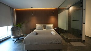 Un dormitorio moderno con una cama grande, una silla, una planta y un área de ducha de vidrio.