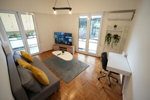Un salon moderne avec un canapé gris, une table basse blanche et un téléviseur posé sur un meuble en bois.