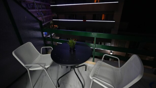 Un balcón con una mesa redonda, dos sillas, una planta en maceta y una barandilla.