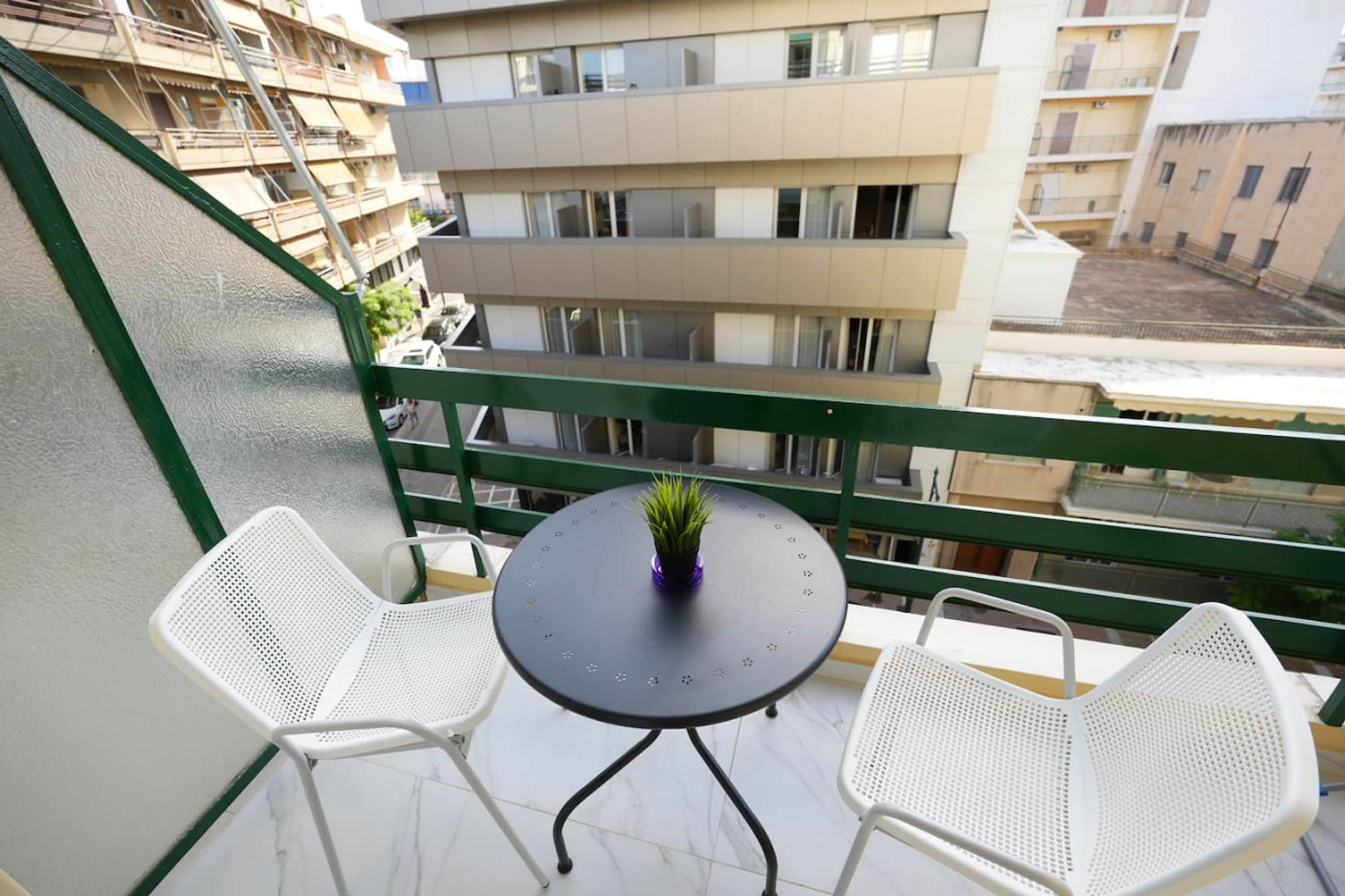 Ein Balkon mit zwei weißen Stühlen und einem Tisch mit einem Blumentopf.