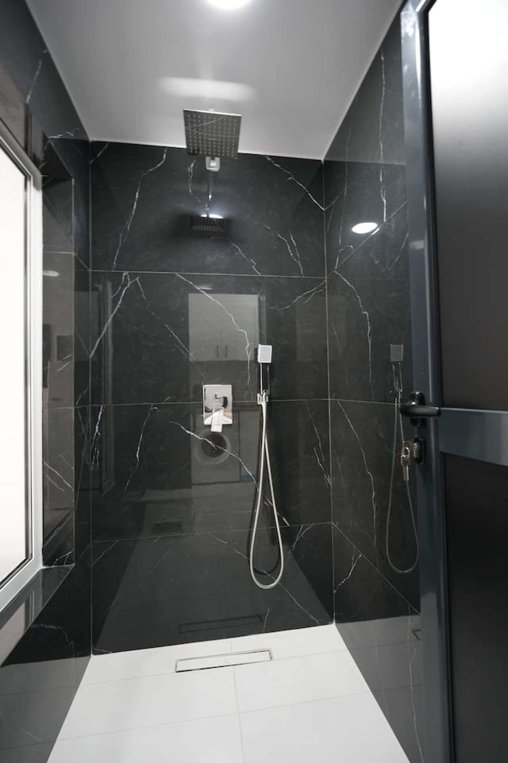 Ein modernes Badezimmer mit Duschkabine aus Glas, Marmorwänden und Fliesenboden.