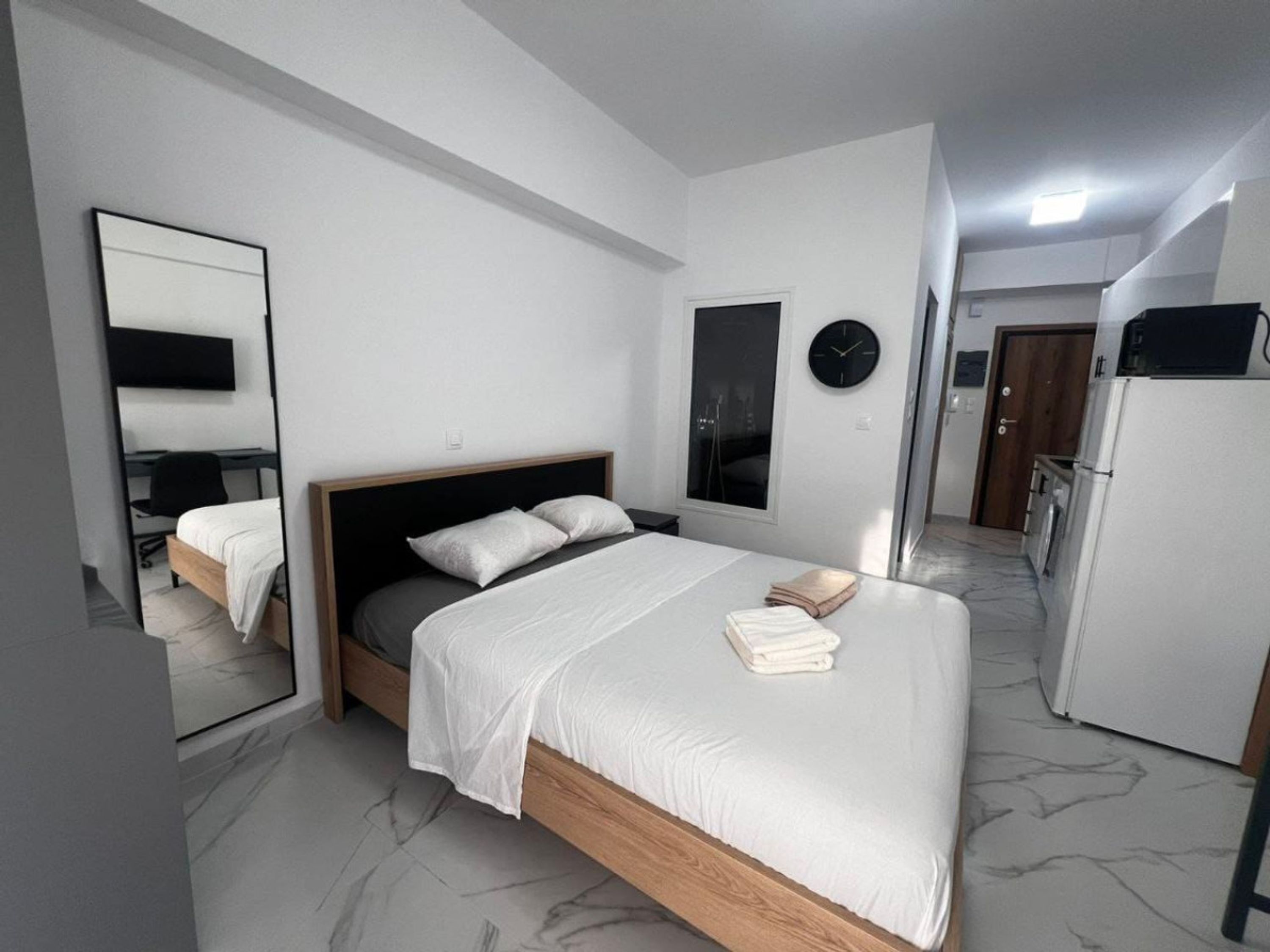 Quarto moderno com cama, espelho, relógio e frigorífico.