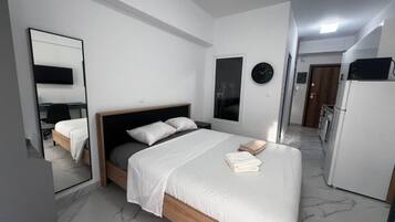 A modern bedroom with a bed, a mirror, a clock, and a refrigerator.