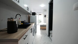 Cocina estrecha con encimera de madera, lavadora y una cama en la habitación contigua.