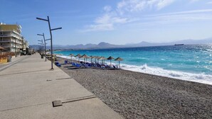 Un paseo marítimo con playa de guijarros, sillas azules para tomar el sol y sombrillas.