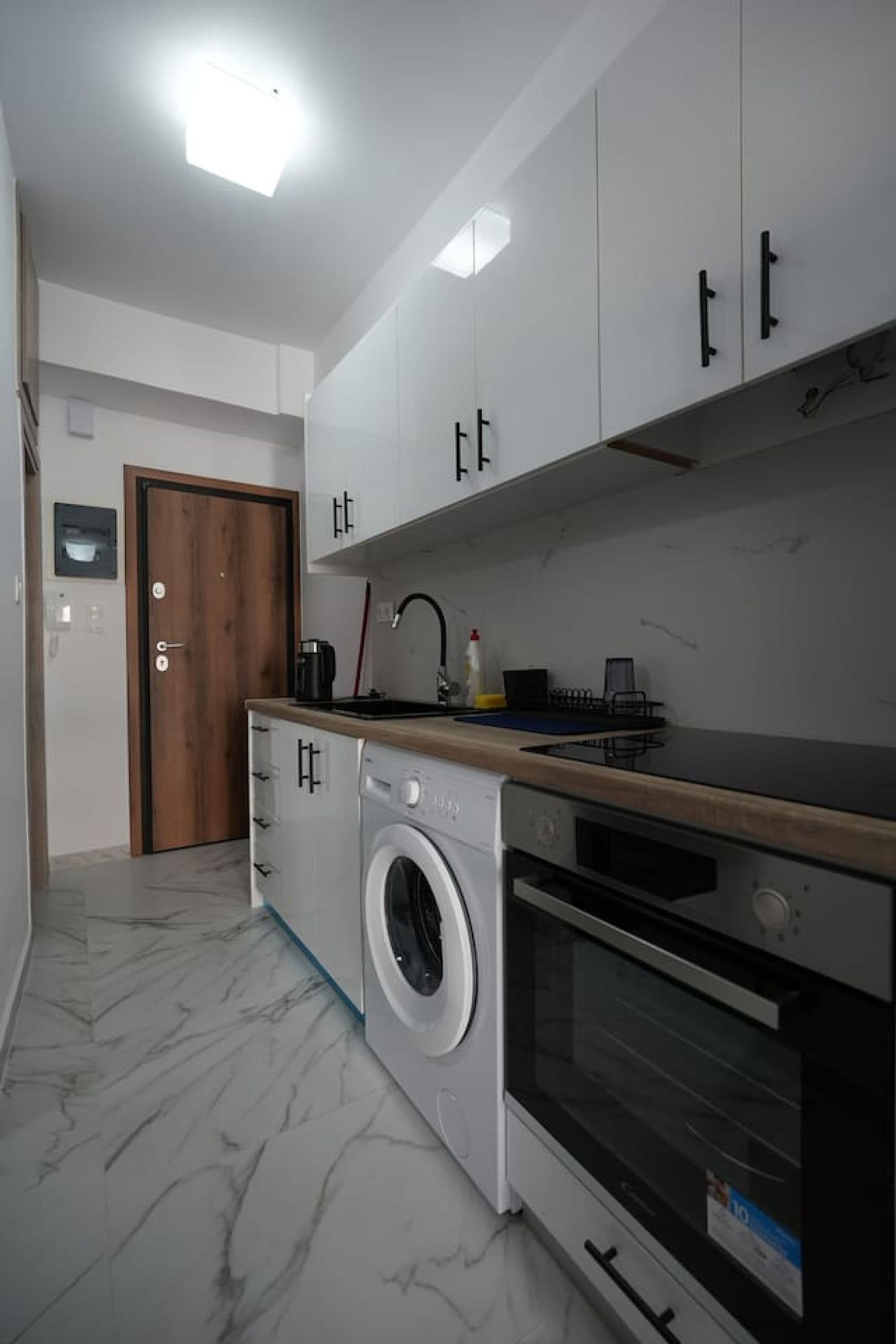 Une cuisine compacte équipée d’un lave-linge, d’un four et d’un plan de travail en bois.