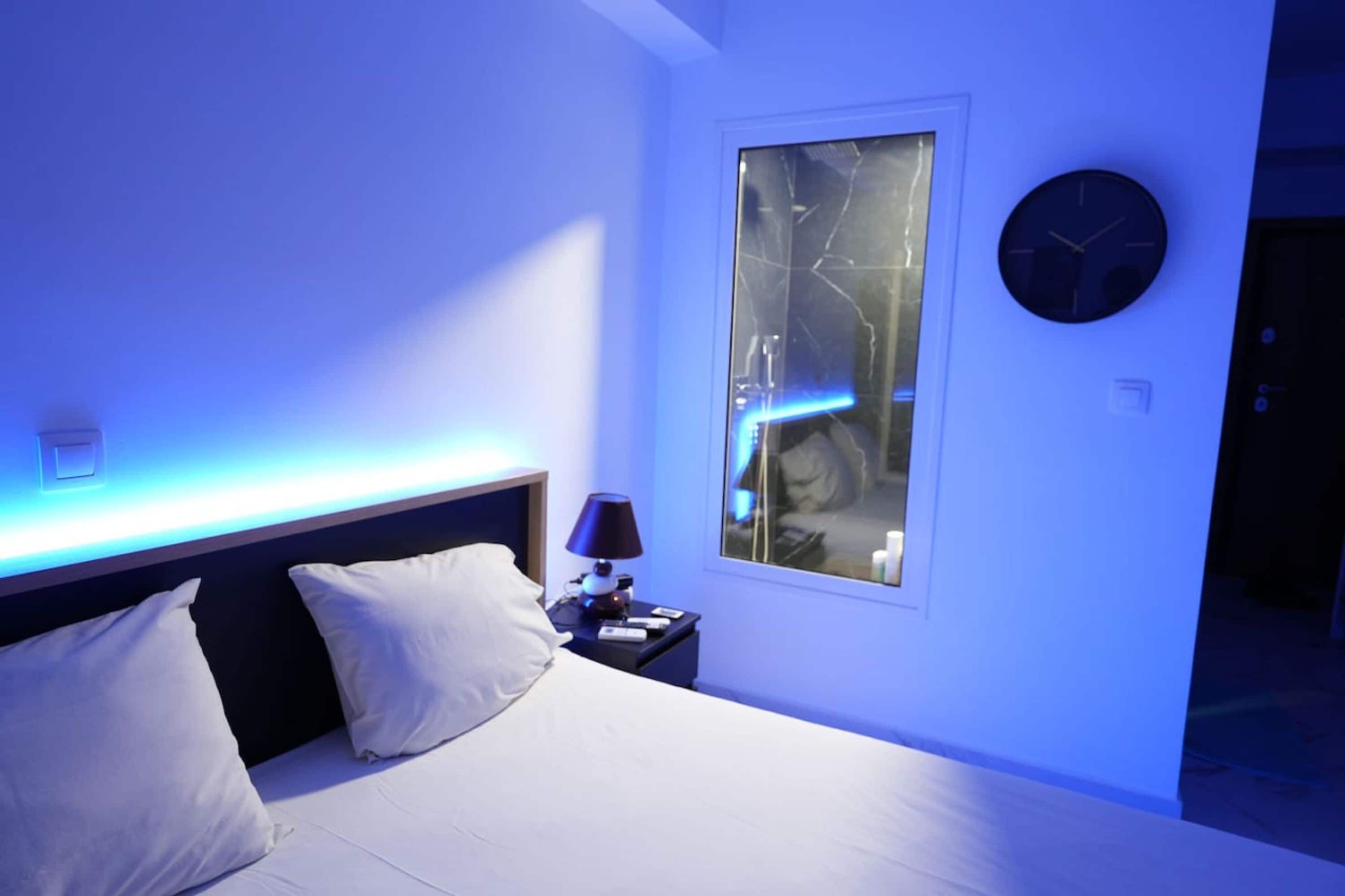 A modern bedroom with a bed, bedside table, lamp, and a clock on the wall.