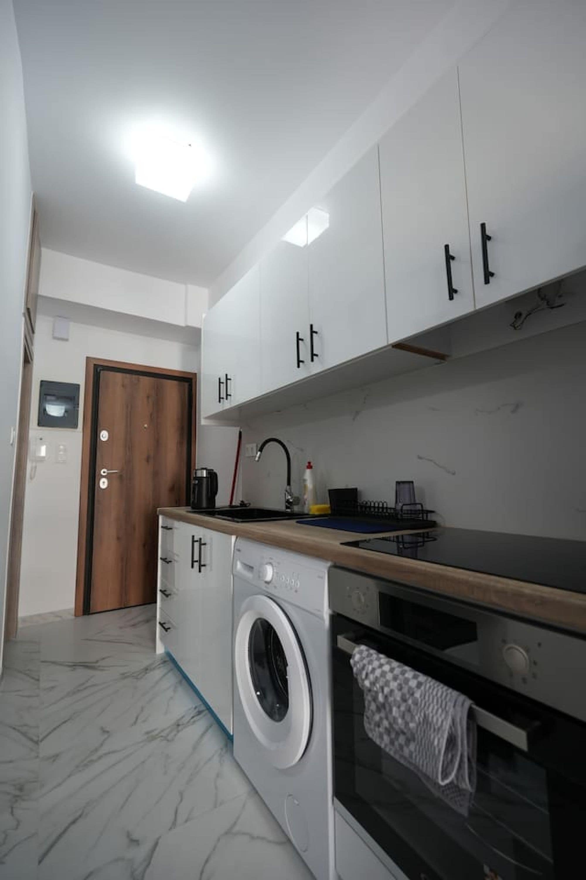 A compact kitchen with white cabinets, a washing machine, and a built-in oven.