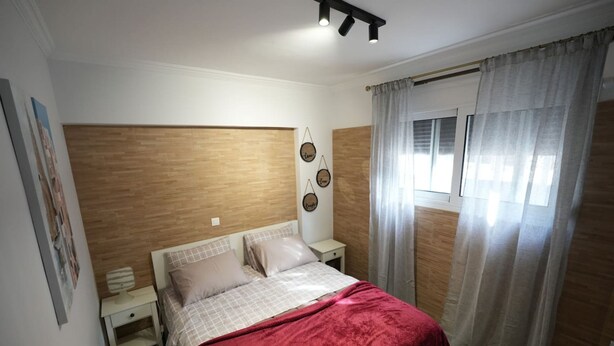 A bedroom with a wooden headboard, a bed with a red blanket, a nightstand, and a window with curtains. - Lovely Front Garden 2 Bdrm Nea Smyrni (Nea Smirni)