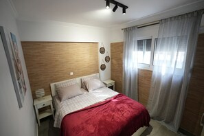 A bedroom with a wooden headboard, a bed with a red blanket, a nightstand, and a window with curtains. - Lovely Front Garden 2 Bdrm Nea Smyrni (Nea Smirni)