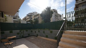 A courtyard with a green mesh fence, a wooden bench, and steps leading to a balcony. - Lovely Front Garden 2 Bdrm Nea Smyrni (Nea Smirni)
