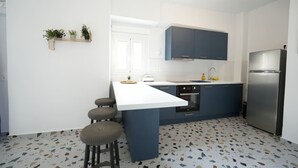 Una cocina moderna con encimera blanca, armarios azul oscuro, refrigerador de acero inoxidable y suelo de terrazo.