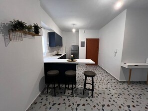 A compact kitchen with a white countertop, two stools, and a refrigerator. - Loutraki Beach Bliss 3 min to Beach (Loutraki-Agioi Theodoroi)