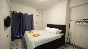 Habitación de hotel con cama, televisión, perchero y aire acondicionado instalado en la pared.