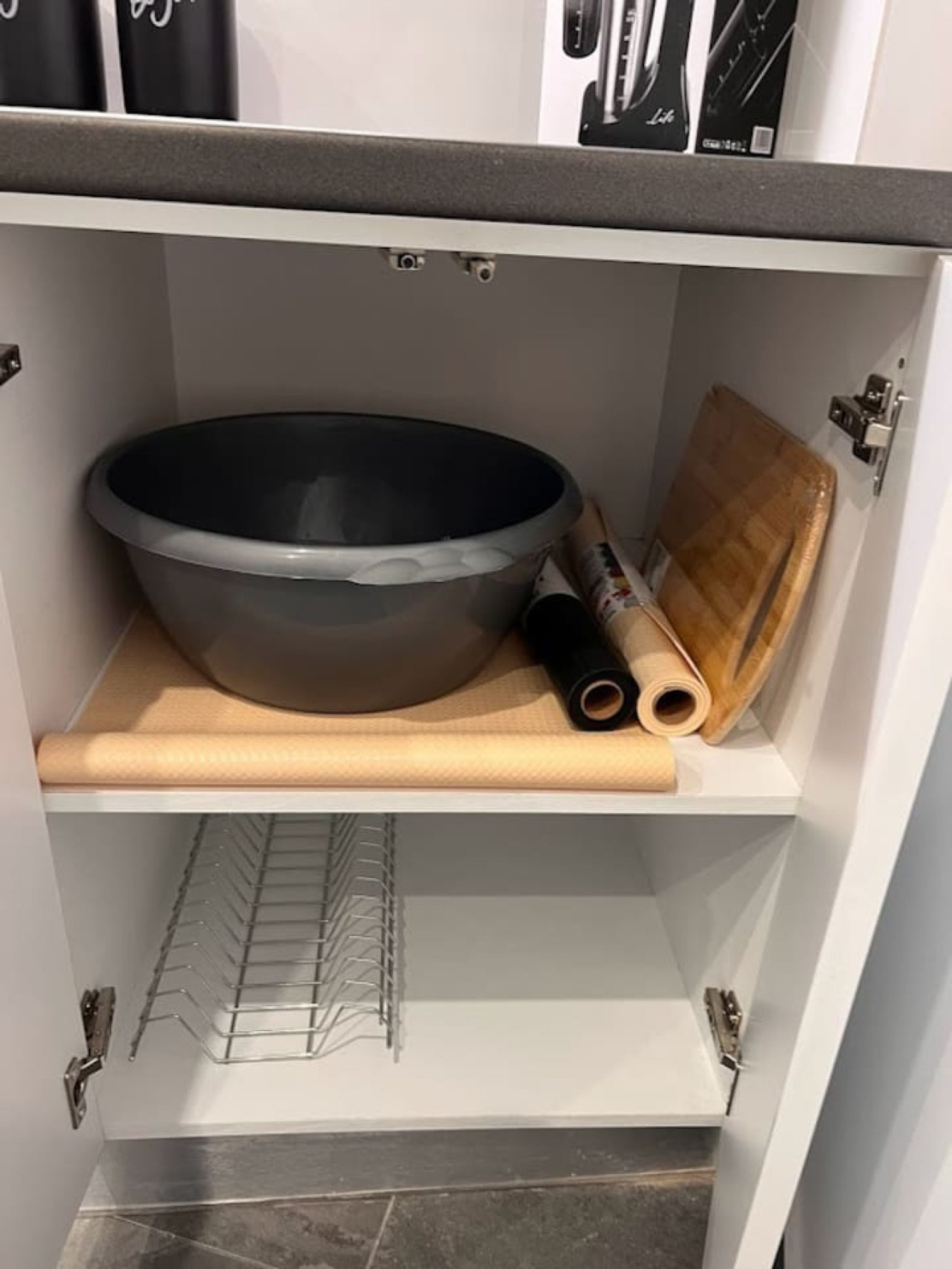 A kitchen cabinet with a large black mixing bowl, wooden rolling pin, and a wooden cutting board.