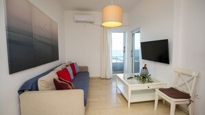 A modern living room with a sofa, a coffee table, a TV, and a view of the sea through a glass door. - Best View Loutraki 2 Bedroom (Loutraki-Agioi Theodoroi)