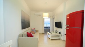 A compact living space with a sofa, a small table, a red refrigerator, and a TV. - Best View Loutraki 2 Bedroom (Loutraki-Agioi Theodoroi)