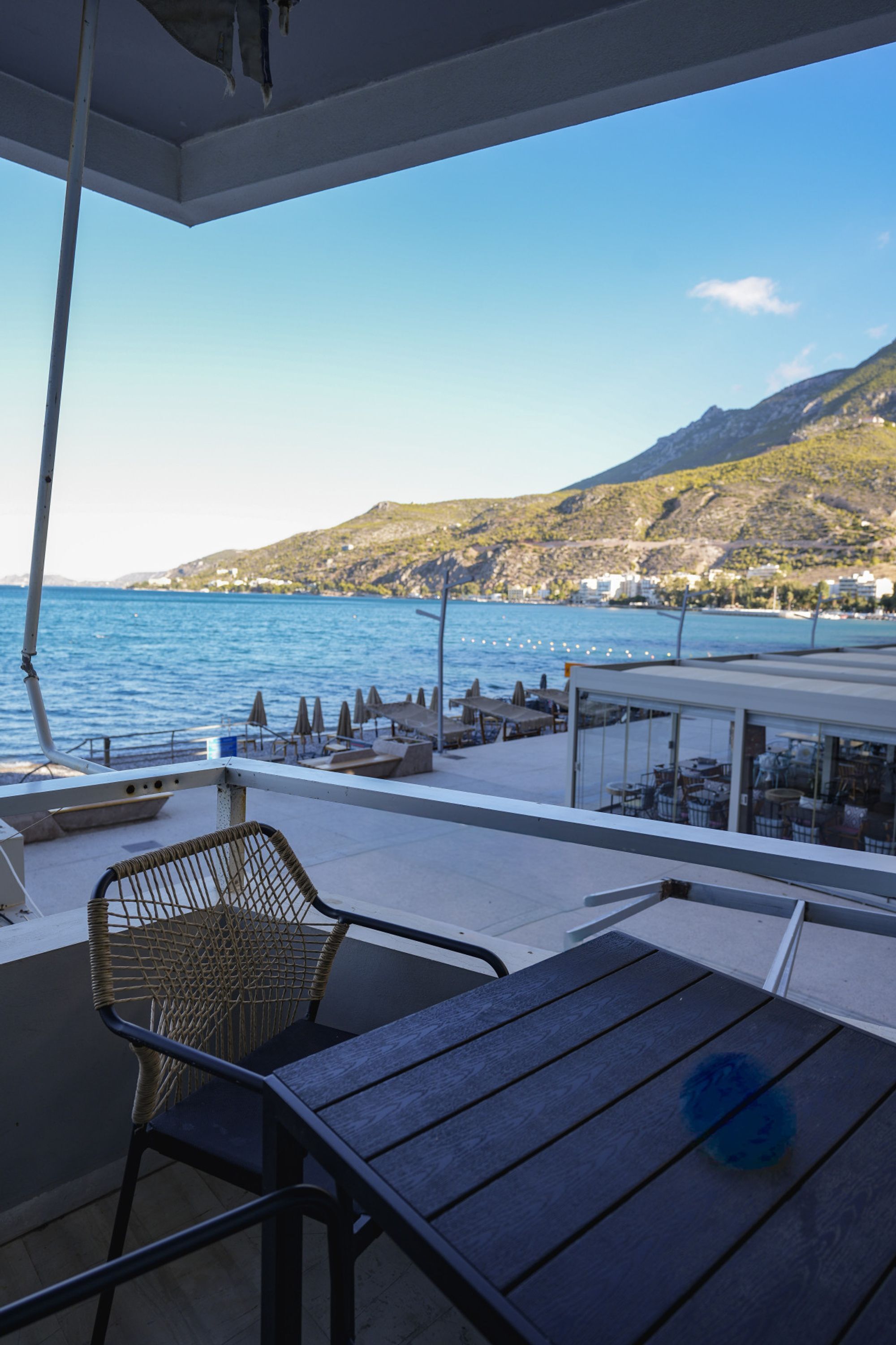 A terrace with a view of the sea and mountains, featuring a table and a wicker chair.