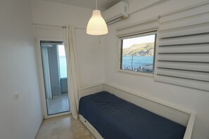 A small, bright room with a bed, a window with a view of the sea, and an air conditioning unit. - Best View Loutraki 2 Bedroom (Loutraki-Agioi Theodoroi)
