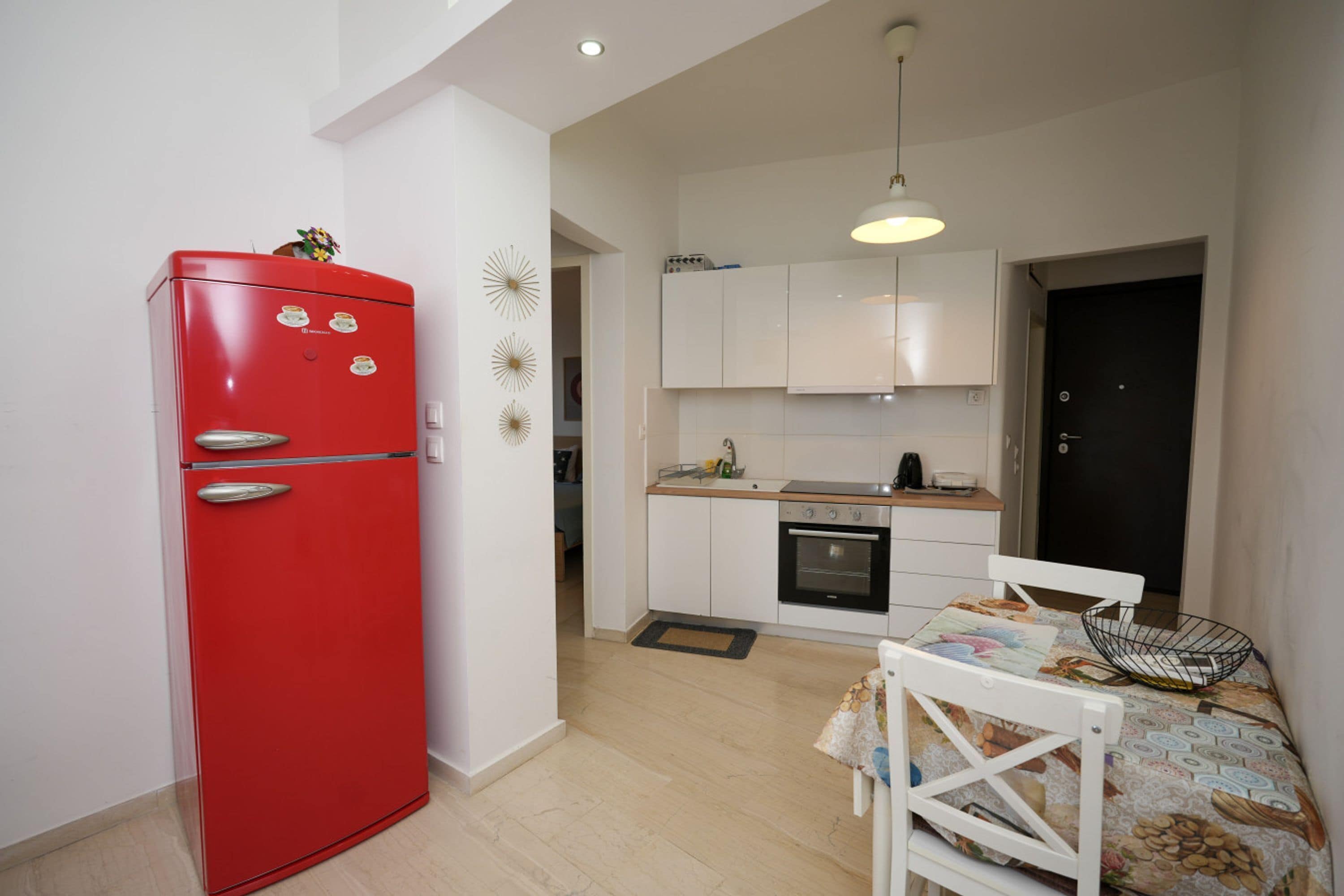 A compact kitchen with a red refrigerator, white cabinets, and a dining area with a white chair and table.
