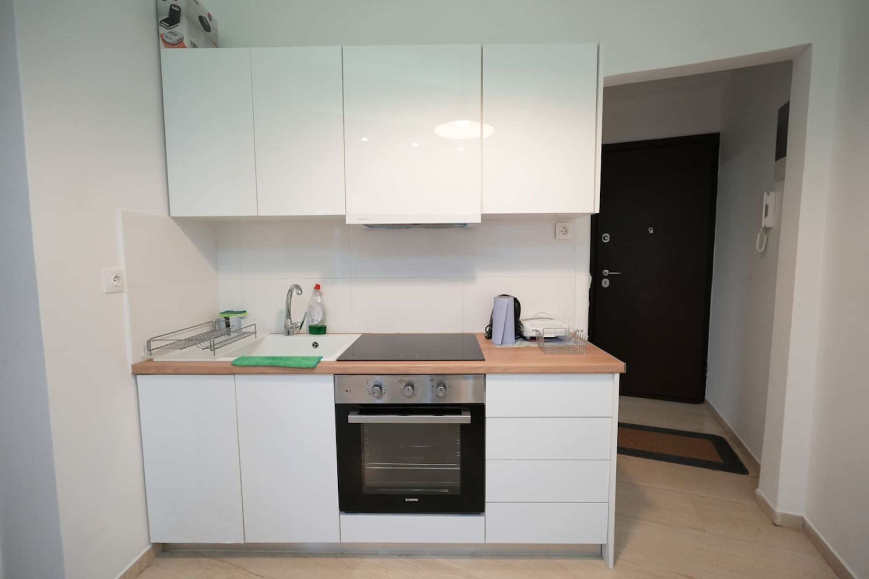A compact kitchen with white cabinets, a built-in oven, and a countertop with a kettle and a small sink.