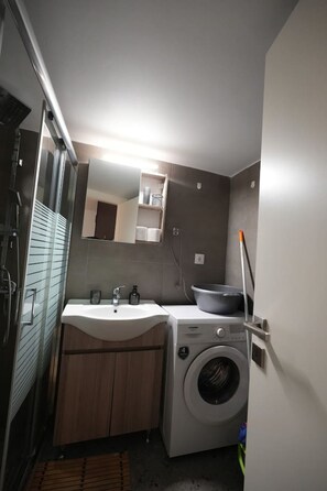 Un bagno compatto con lavandino, specchio e lavatrice.