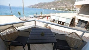A balcony with a table and two chairs, overlooking a coastal area with buildings and a view of the sea. - Best View Loutraki 2 Bedroom (Loutraki-Agioi Theodoroi)