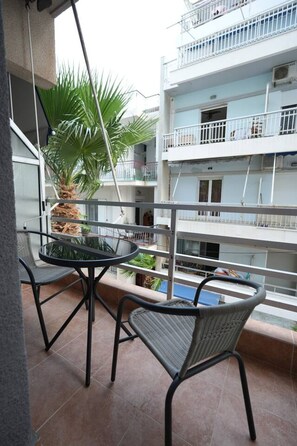 Un balcón con mesa y sillas, una planta en maceta y vista a un edificio de varios pisos con balcones.