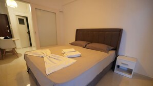 Una cama bien hecha con un cabecero marrón, una mesita de noche pequeña y una mesita auxiliar blanca.