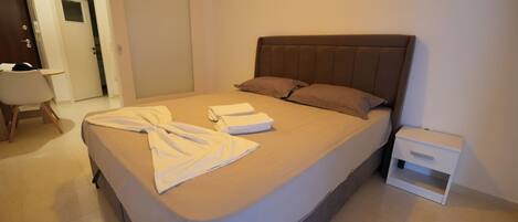 A neatly made bed with a brown headboard, a small bedside table, and a white nightstand.