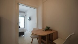 A small, modern room with a wooden dining table, two white chairs, a small plant on the table, and a bed in the background. - Beachfront Escape Seaview (Loutraki-Agioi Theodoroi)