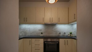 A kitchen with beige cabinets, a black oven, and a countertop with a plant and a kettle. - Beachfront Escape Seaview (Loutraki-Agioi Theodoroi)