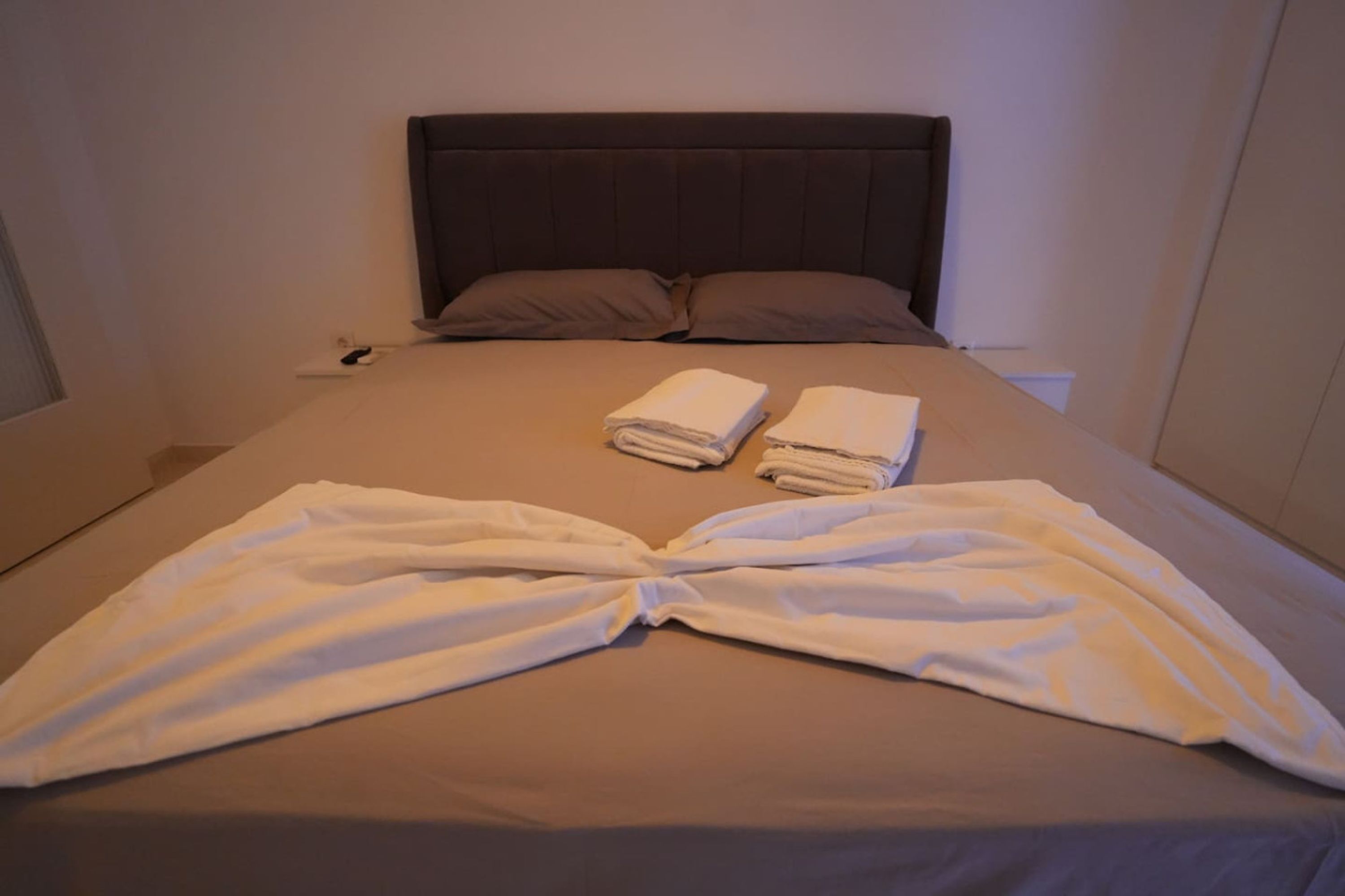A neatly made bed with a folded white towel and a towel arranged in a heart shape.