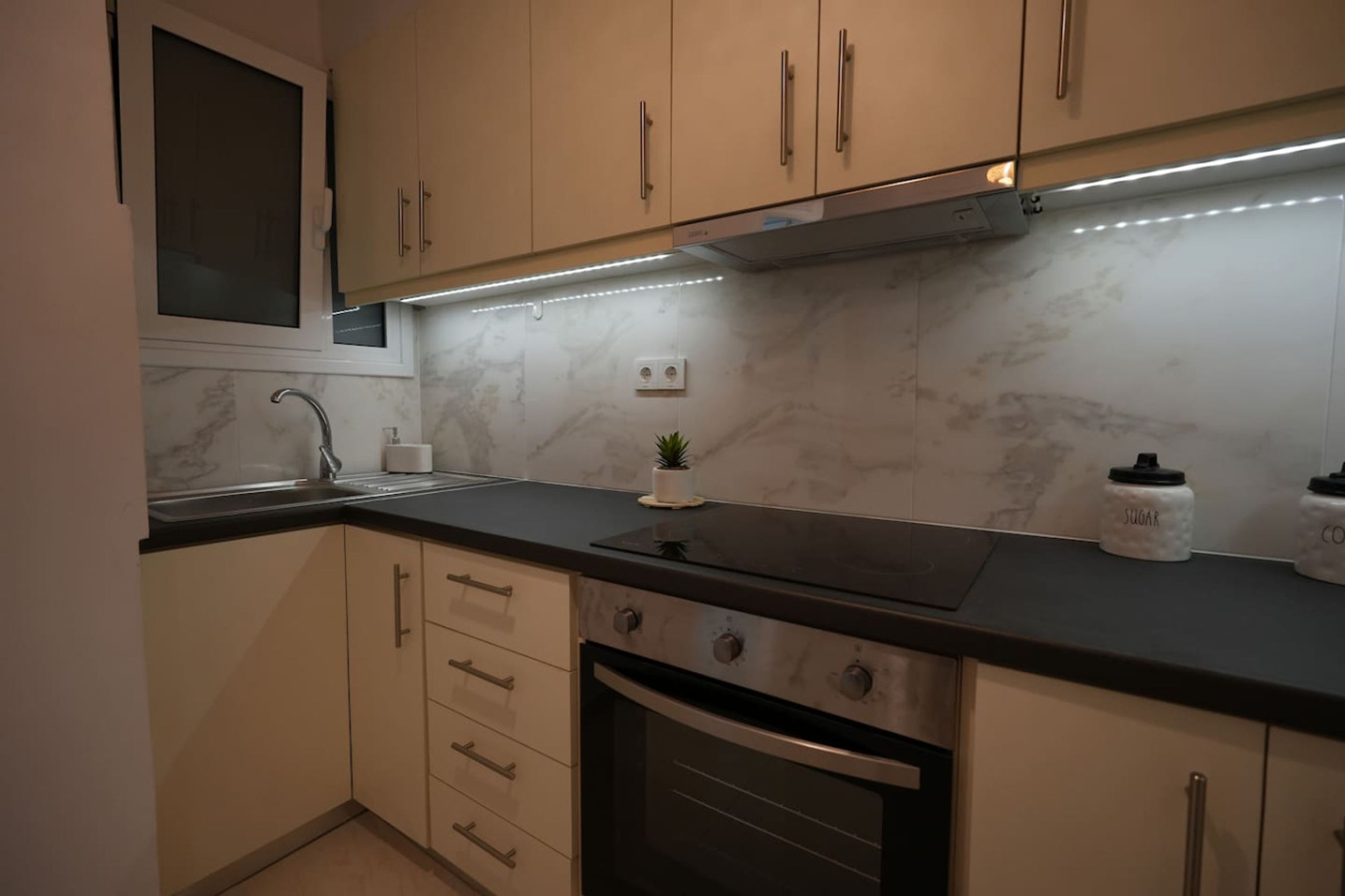 A modern kitchen with beige cabinets, a black countertop, a built-in oven, and a stainless steel range hood.