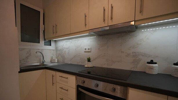 Una cocina moderna con armarios color beige, encimera negra, horno empotrado y campana extractora de acero inoxidable.