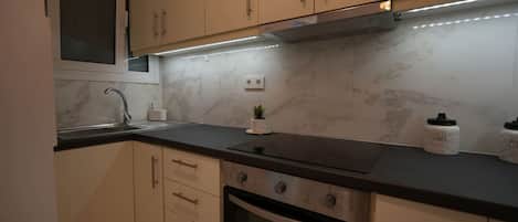 A modern kitchen with beige cabinets, a black countertop, a built-in oven, and a stainless steel range hood.