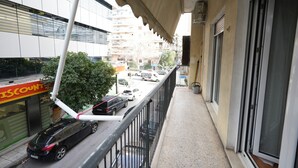 Un balcone con vista su una strada, un edificio con un negozio a prezzi scontati e un'auto parcheggiata.
