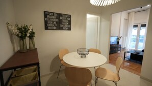 Zona pranzo con tavolo rotondo e quattro sedie, insegna a parete che elenca diverse località e lampadario decorativo.