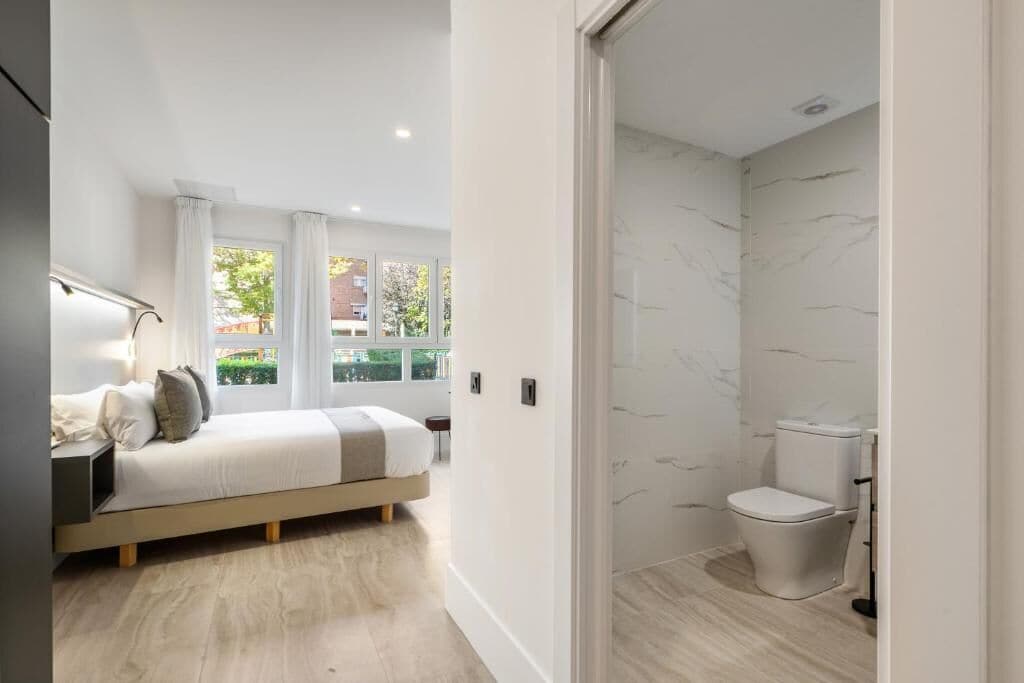 Un dormitorio moderno con cama, mesita de noche y vistas al exterior.