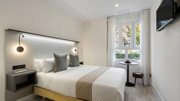 Ett modernt hotellrum med en stor säng, sängbord, en tv som är monterad på väggen och ett fönster med utsikt över grönområden.
