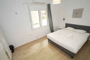 A bedroom with a bed, a window, a wall-mounted air conditioner, and a small bedside table. - Central 1 Bdrm Apartment in Pangrati (Athens)