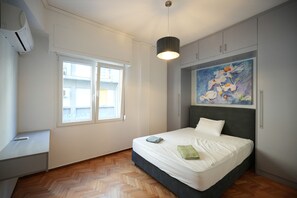 Un dormitorio con cama, ventana, equipo de aire acondicionado y un cuadro en la pared.