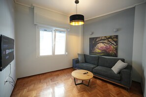 Una sala de estar con un sofá gris, una mesa redonda de centro, un cuadro en la pared y una lámpara de techo.