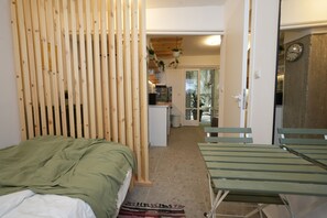Une chambre avec un lit, une cloison en bois, un canapé vert et une vue sur une cuisine et un balcon.