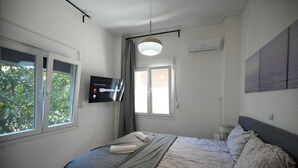 Ein Schlafzimmer mit einem Bett, einem Fernseher an der Wand und einem Fenster mit Vorhängen.