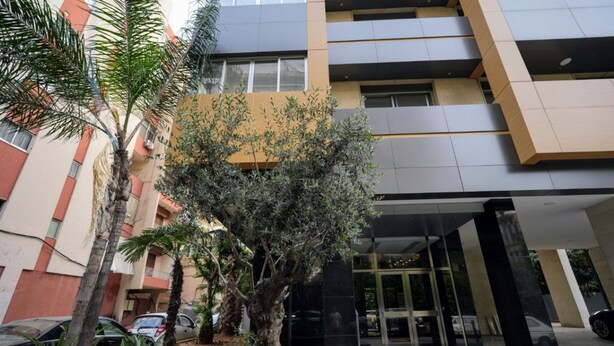 A modern building with a glass entrance, surrounded by palm trees and a small garden area. - The Purple Apartment Badaro 3 Bdrm 24 7 Electric (Beirut)